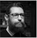 A man with a beard and glasses is looking at the camera.